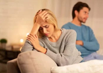 A unhappy woman sitting with her boyfriend with her hand on her face.